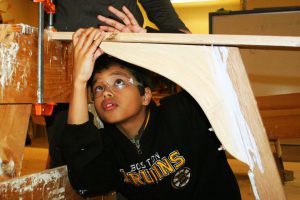 A boy measuring part of a boat he is building