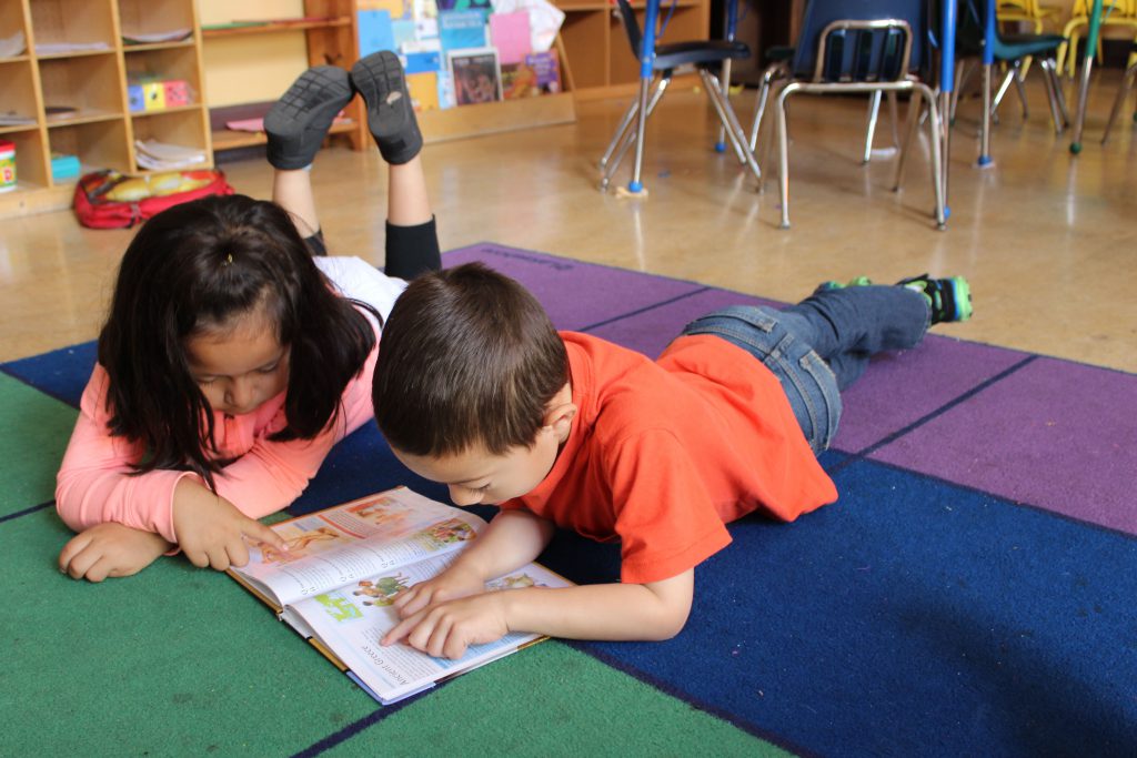 A boy and a girl lying on mats, reading