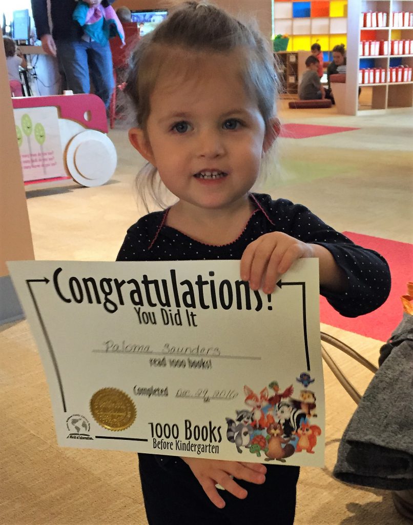 Little girl holds book she won for completing 1000 Books Before Kindergarten