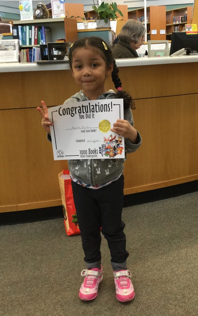 Little girl holds book she won for completing 1000 Books Before Kindergarten