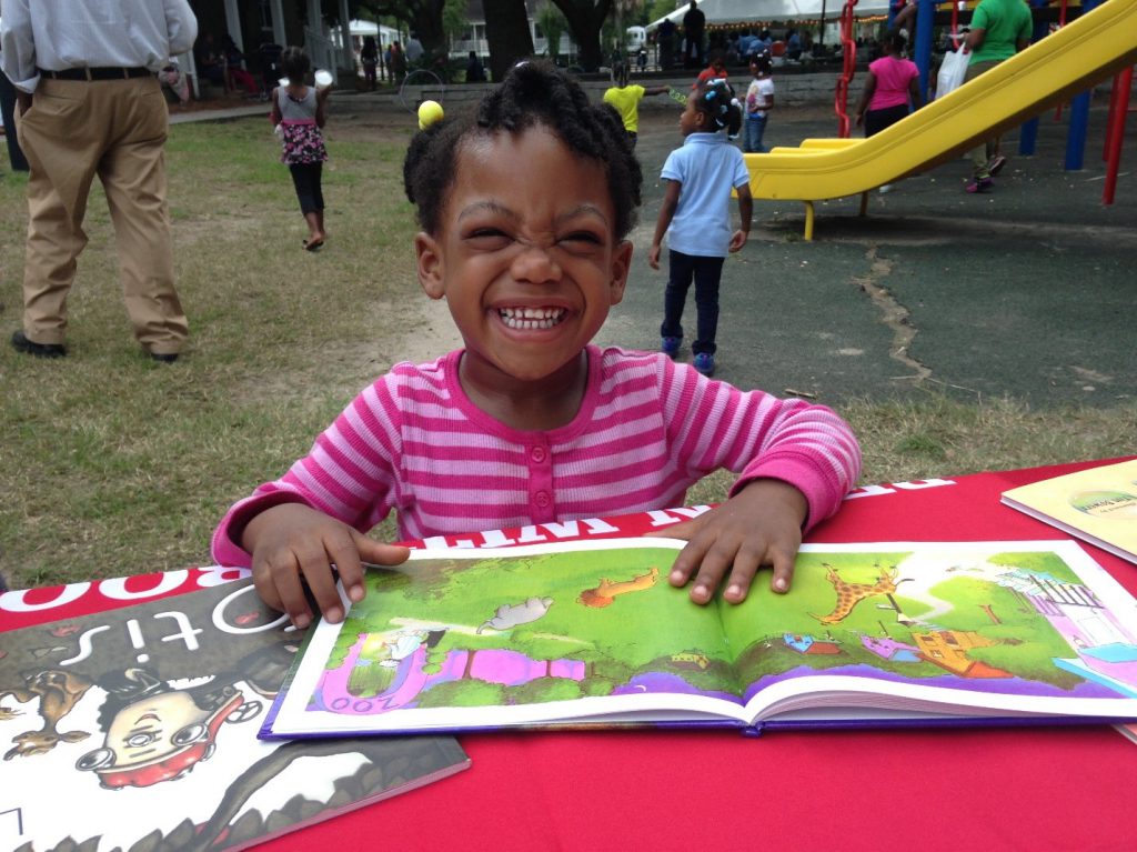 Grinning child looks at a storybook at a BEGIN WITH BOOKS presentation in a local park