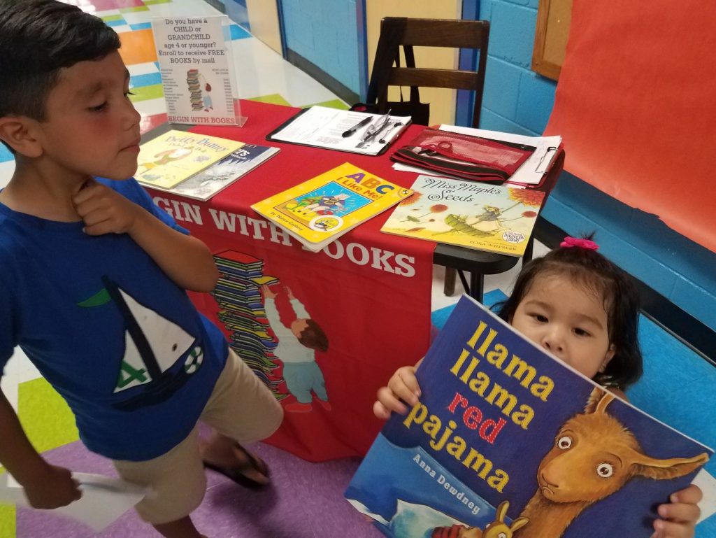 Small Asian girl looks at storybook as big brother looks on