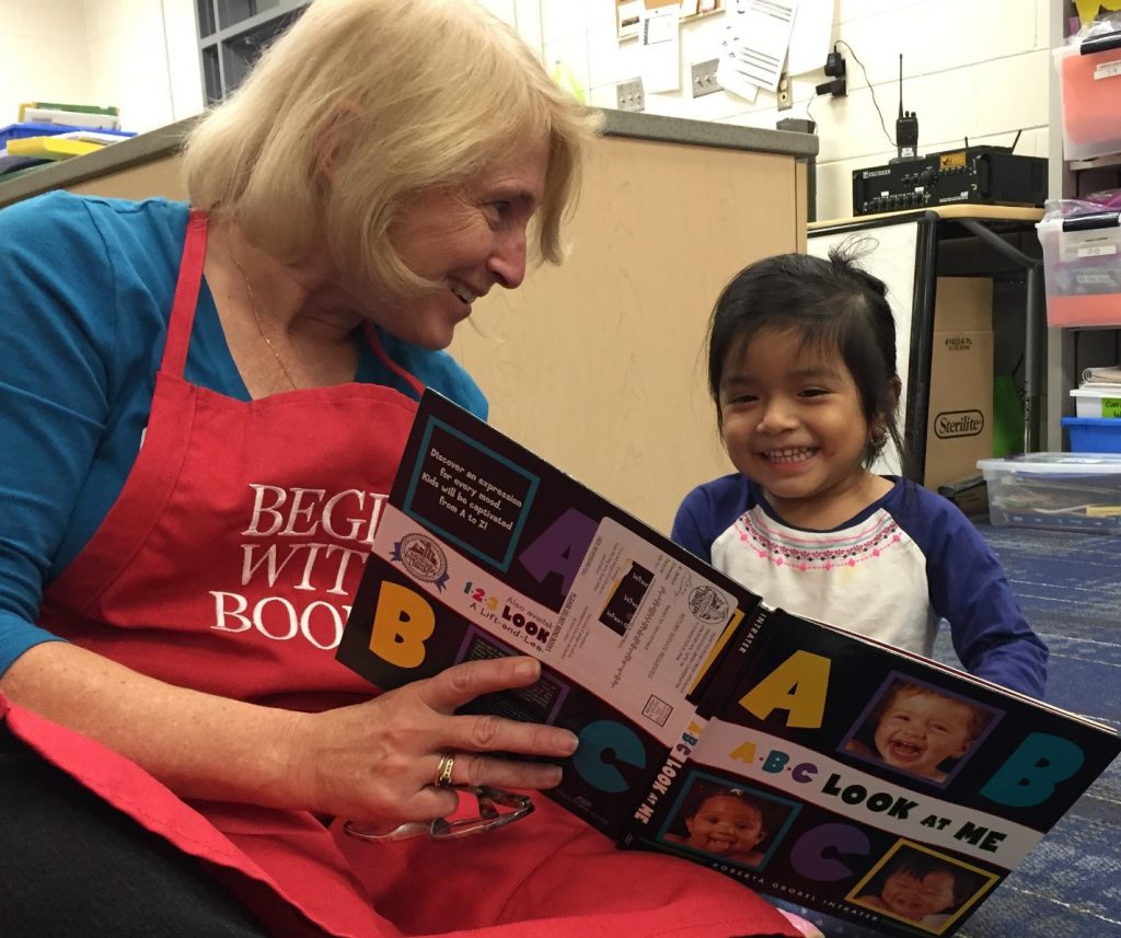 Smiling volunteer reads book to young child