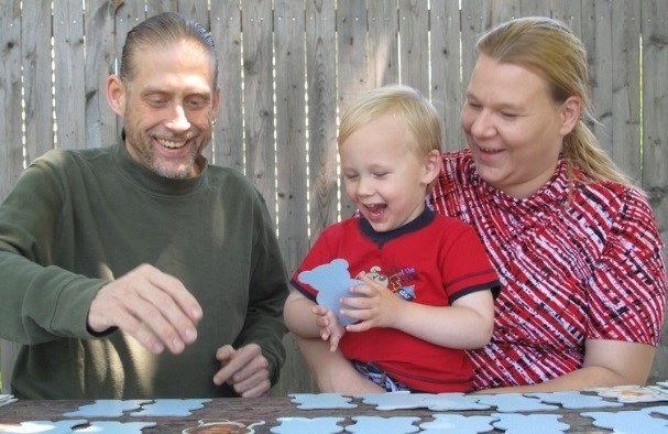 Child plays game with two smiling adults (Child-Parent Home Program)