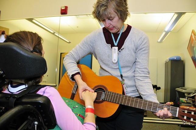 Music therapist aids helps young patient strum a guitar