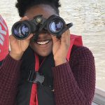 Smiling Green Works student looks through binoculars