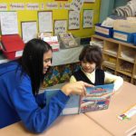 older girl reads to younger girl