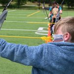 young blonde boy practices archery at the Y