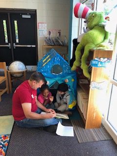 Male volunteer reads to two children sitting in play tent, Everybody Wins! Atlanta