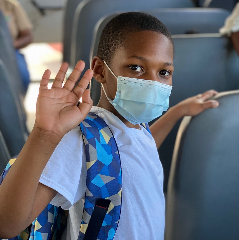 Masked boy on school bus to Horton's Kids,waves