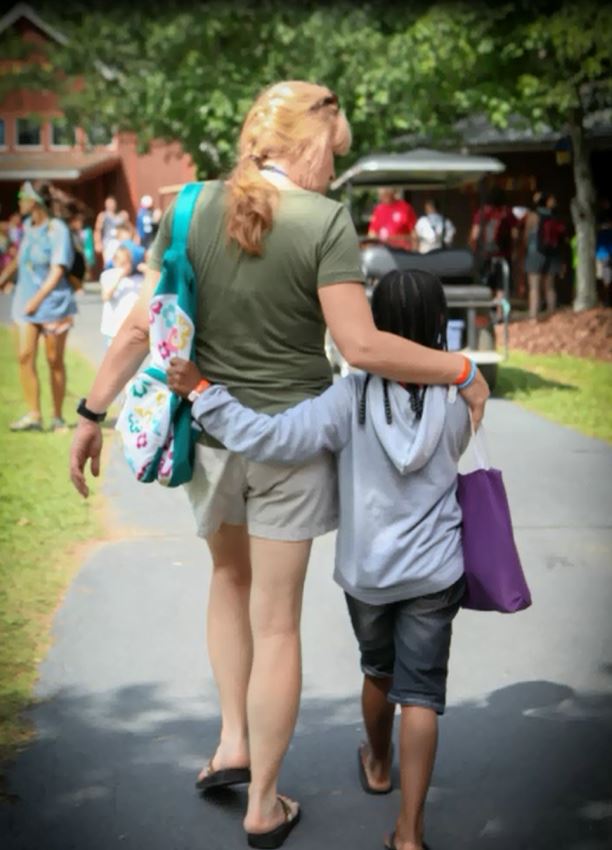 volunteer and child walk with arms around each other