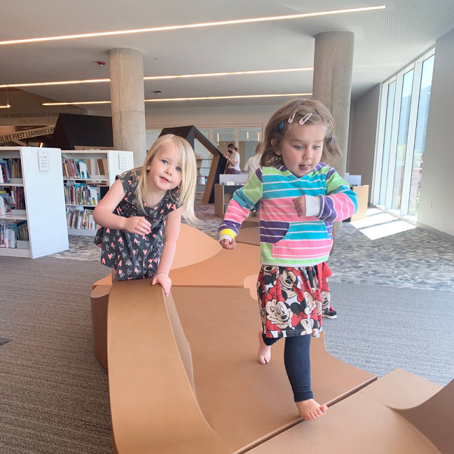 Girls play on wooden climbing toys in Families First library