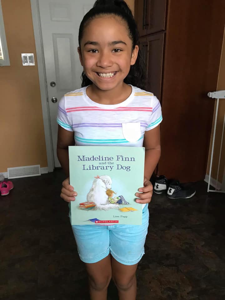 Lilianna smiles, holds book from 501c3 Kids Read Now
