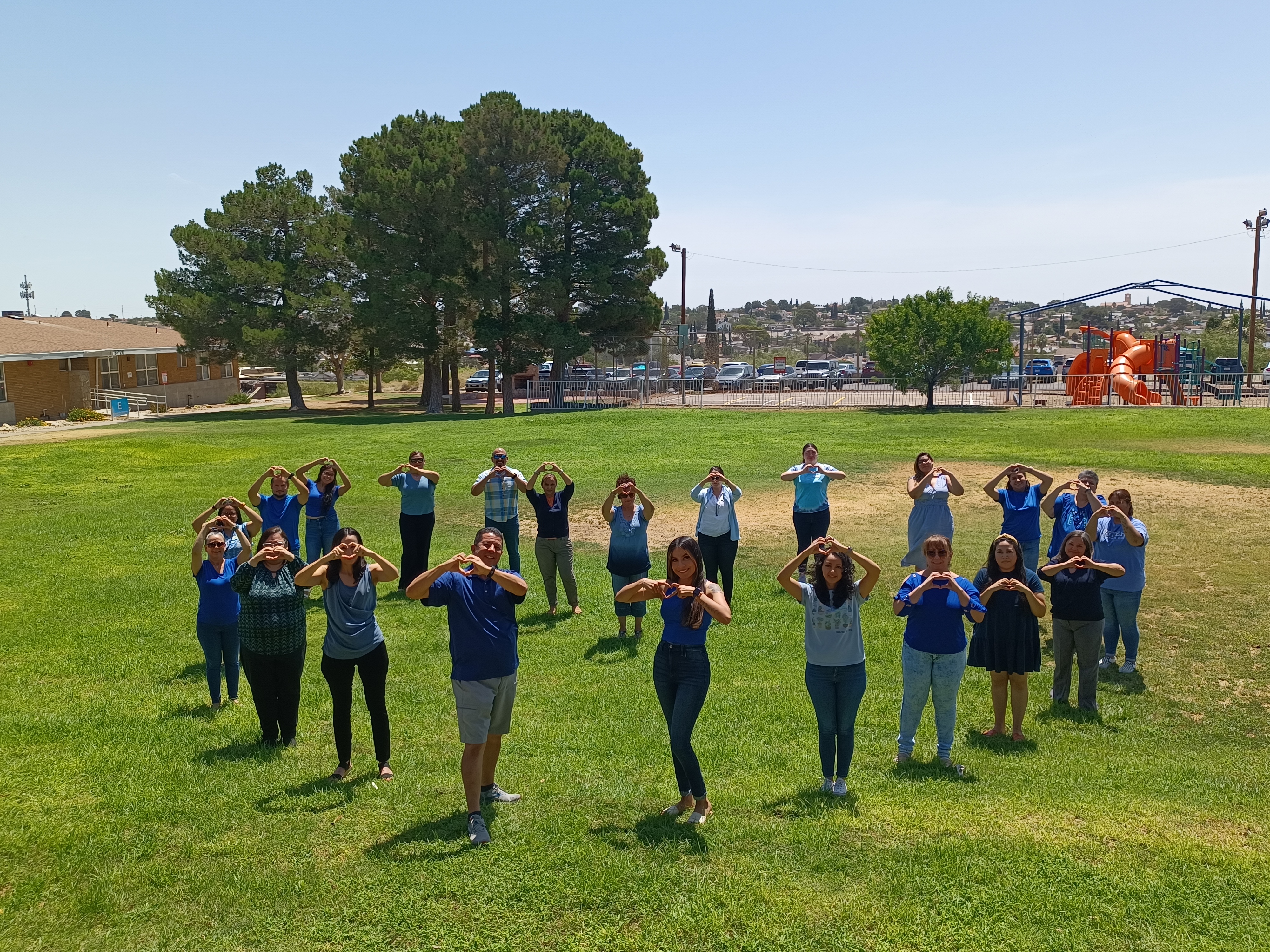 Group of people standing on grass making heart shapes with their hands, showing unity and support.