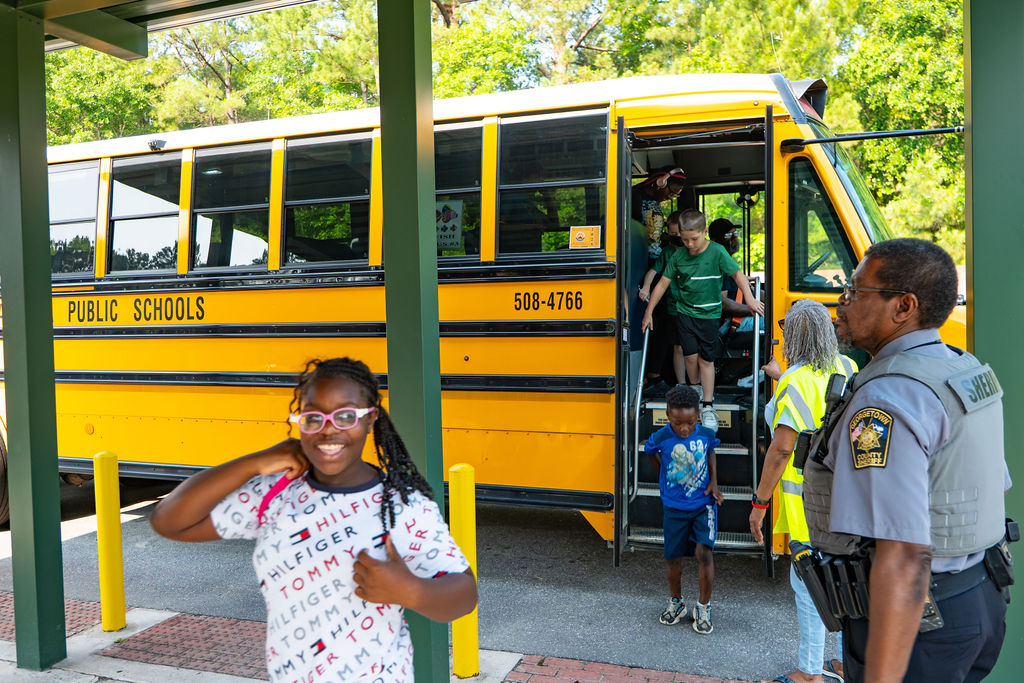 smiling black girl leaving school bus to go to The Village Group