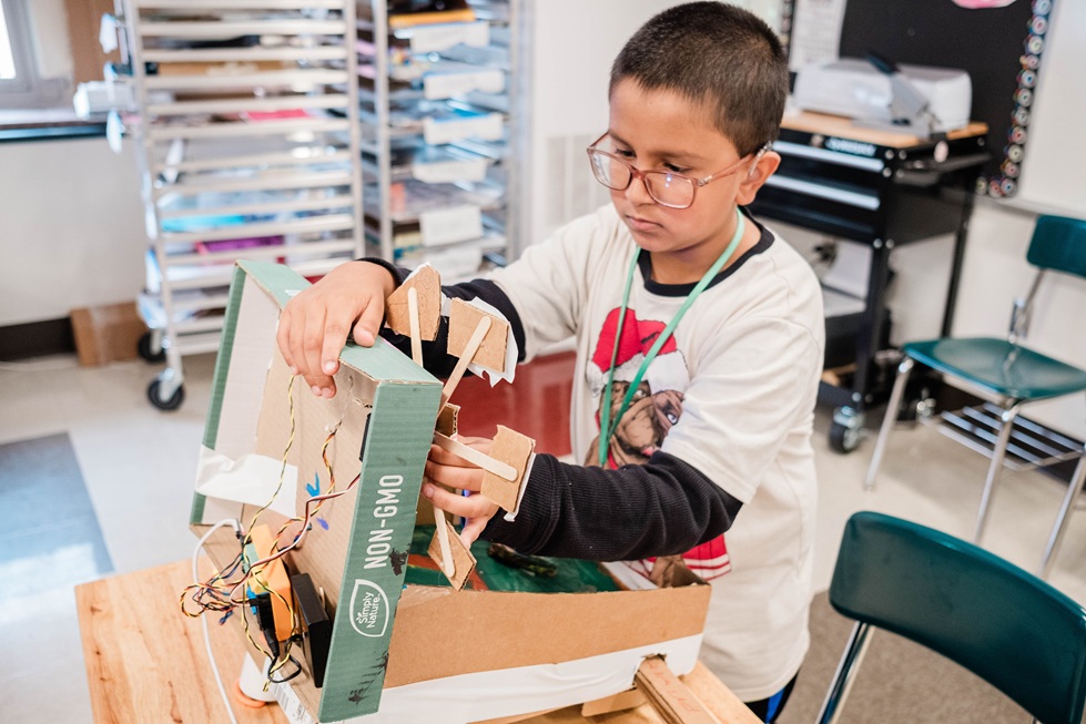 Hands-on problem-solving: A student builds and tests a cardboard engineering project, learning how physical design and coding work together.