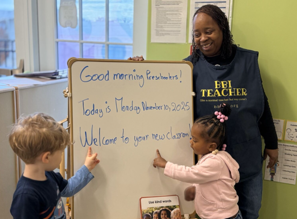 Children and teacher point and read welcome sign