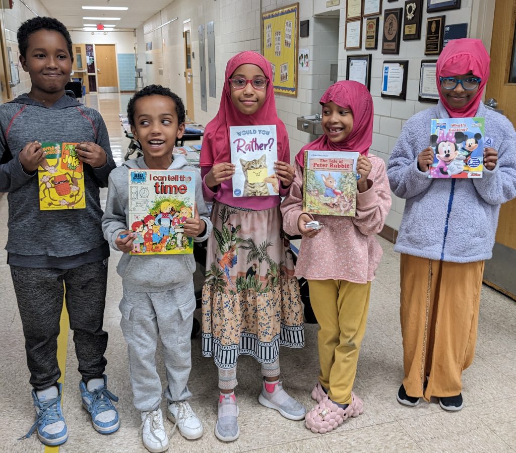 2 boys, 3 girls in hijabs, smiling, holding books