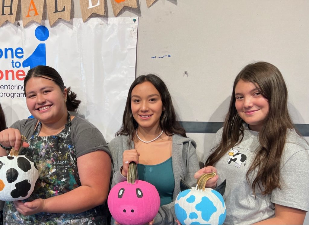 Three girls hold their decorated pumpkins one to one mentoring