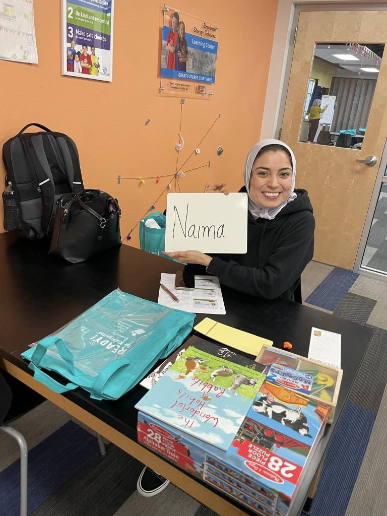 smiling woman in hijab holds up card reading Naima