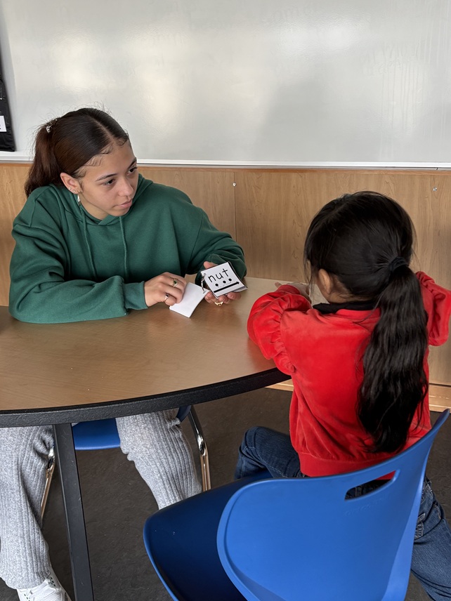 older student uses reading flashcards with younger student